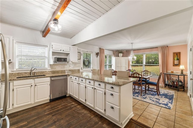 kitchen with light stone countertops, appliances with stainless steel finishes, a peninsula, white cabinets, and a sink