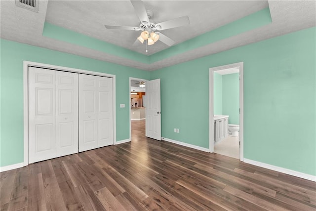 unfurnished bedroom with dark wood-type flooring, ceiling fan, a raised ceiling, and a closet