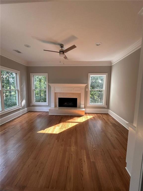 unfurnished living room featuring a premium fireplace, crown molding, dark hardwood / wood-style floors, and a wealth of natural light