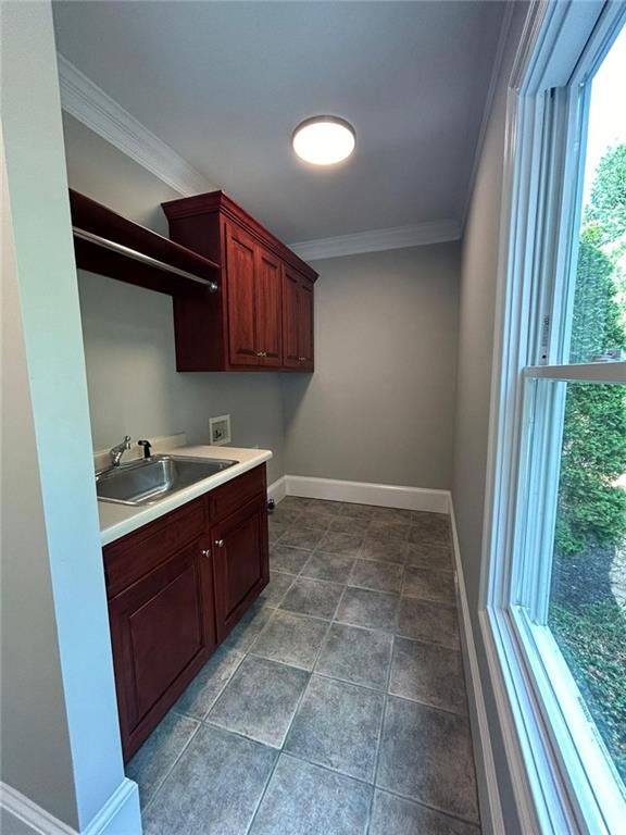 washroom featuring sink, hookup for a washing machine, ornamental molding, and cabinets