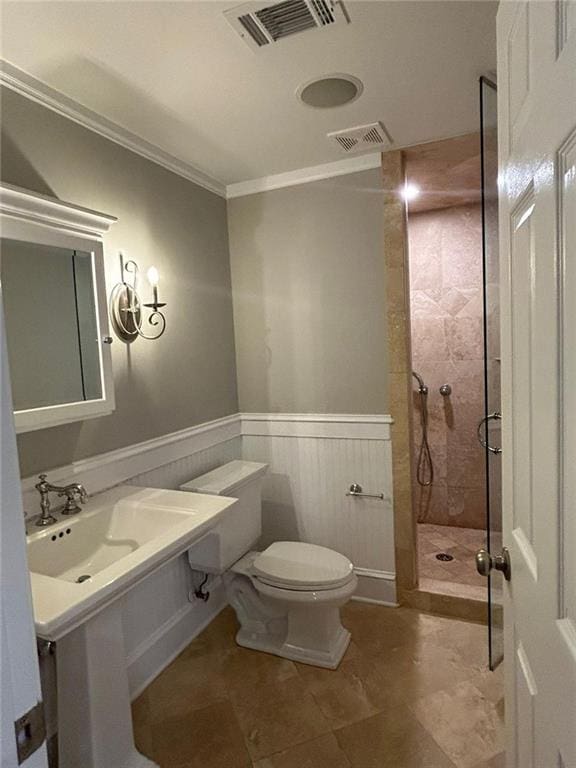 bathroom with ornamental molding, toilet, and tiled shower