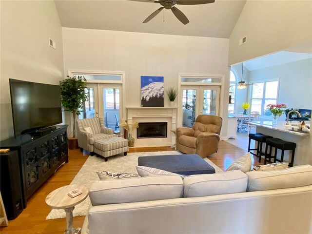 living room with ceiling fan, high vaulted ceiling, and light hardwood / wood-style flooring