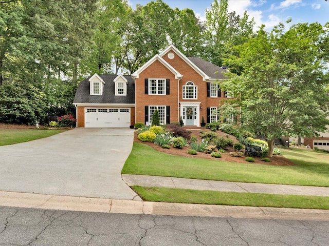 view of front of house with driveway, brick siding, a front lawn, view of wooded area, and an attached garage