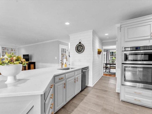 kitchen with a sink, stainless steel appliances, ornamental molding, gray cabinets, and light countertops