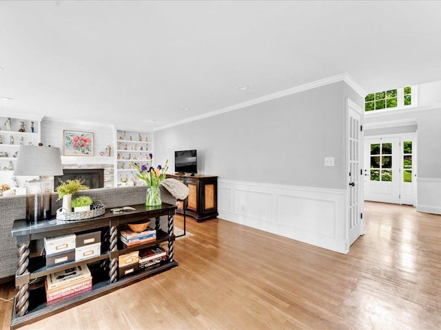 living room featuring a fireplace, wood finished floors, built in shelves, wainscoting, and ornamental molding