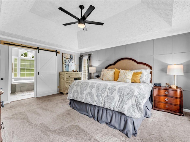 bedroom featuring carpet flooring, a textured ceiling, a barn door, a ceiling fan, and ensuite bath