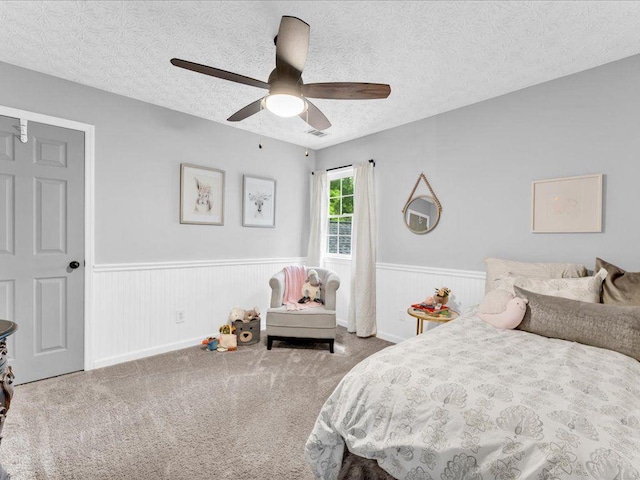 bedroom featuring wainscoting, a textured ceiling, ceiling fan, and carpet floors