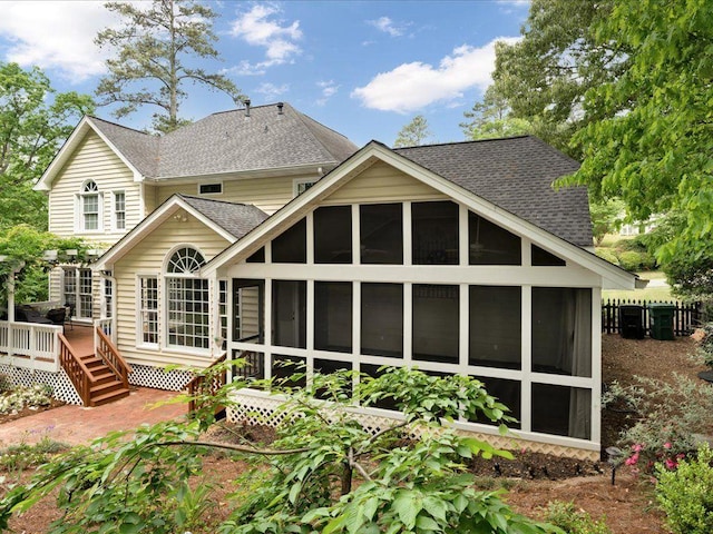 rear view of property featuring a sunroom, a shingled roof, and a wooden deck