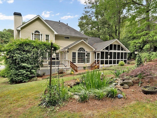 rear view of property featuring a sunroom, a deck, a chimney, and roof with shingles