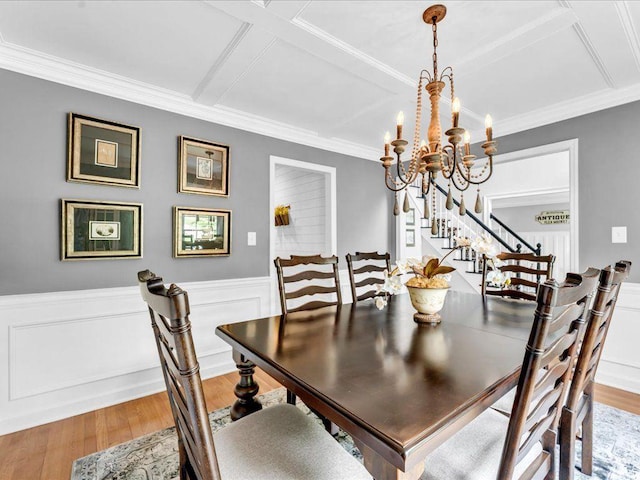 dining area featuring light wood-style flooring, stairs, a chandelier, coffered ceiling, and a wainscoted wall