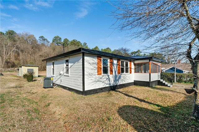 view of side of home with a storage unit, a yard, and central air condition unit