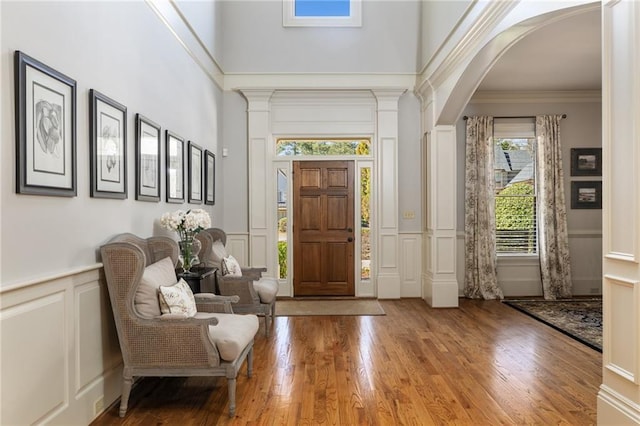 foyer entrance with crown molding, wainscoting, hardwood / wood-style flooring, arched walkways, and a decorative wall