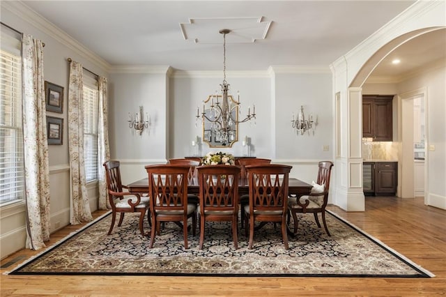 dining room featuring arched walkways, a notable chandelier, wood finished floors, and crown molding