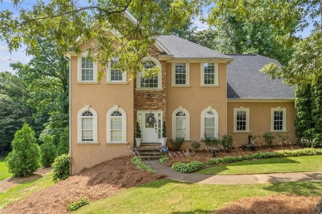 colonial house with stone siding, stucco siding, and a shingled roof