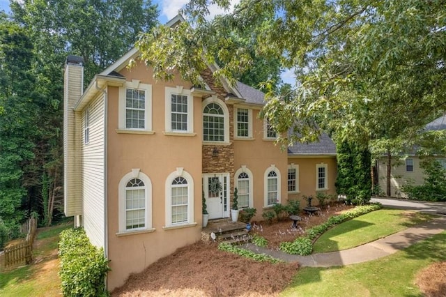 colonial-style house with stucco siding, a chimney, and a shingled roof