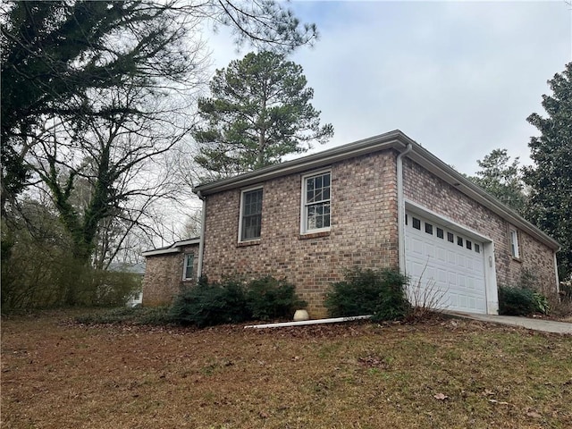 view of side of home featuring driveway, brick siding, and an attached garage