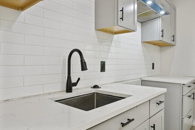 kitchen with light stone counters, sink, backsplash, and extractor fan