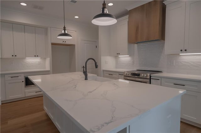 kitchen with an island with sink, hanging light fixtures, and wall chimney range hood