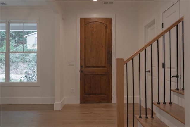 foyer entrance with light wood-type flooring, crown molding, and a healthy amount of sunlight