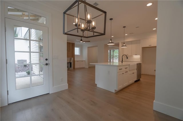 kitchen with a center island with sink, decorative light fixtures, white cabinetry, and sink