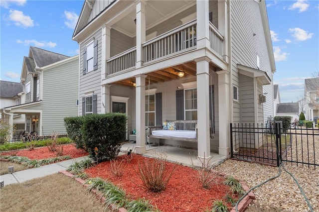 view of property exterior with board and batten siding, a balcony, covered porch, and fence