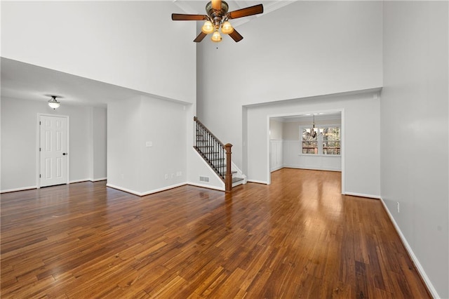 unfurnished living room featuring dark wood-style floors, ceiling fan with notable chandelier, visible vents, and stairs