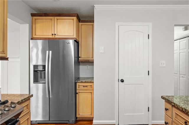 kitchen with stainless steel fridge, ornamental molding, dark stone counters, and a textured ceiling