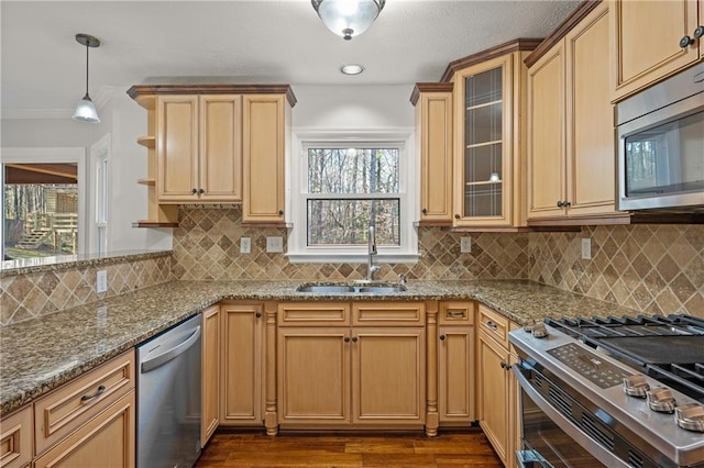 kitchen featuring light stone counters, decorative light fixtures, stainless steel appliances, a sink, and glass insert cabinets