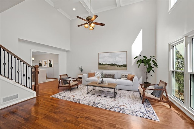 living area featuring visible vents, a towering ceiling, wood finished floors, stairs, and beam ceiling