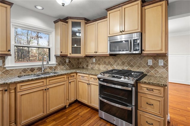 kitchen featuring dark wood-style floors, glass insert cabinets, appliances with stainless steel finishes, light stone countertops, and a sink