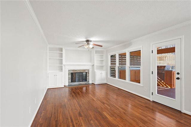 unfurnished living room featuring built in shelves, wood finished floors, baseboards, a brick fireplace, and crown molding