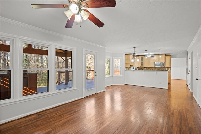 unfurnished living room with baseboards, ornamental molding, ceiling fan, and wood finished floors