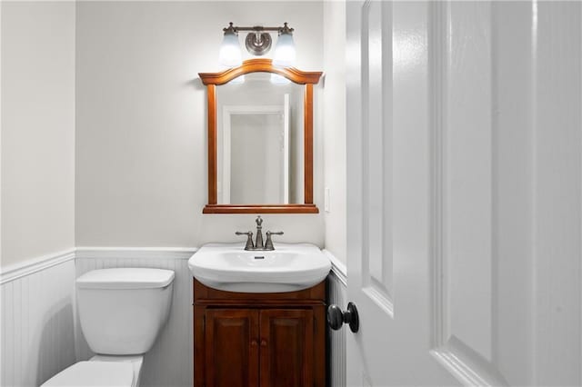 half bathroom featuring wainscoting, vanity, and toilet