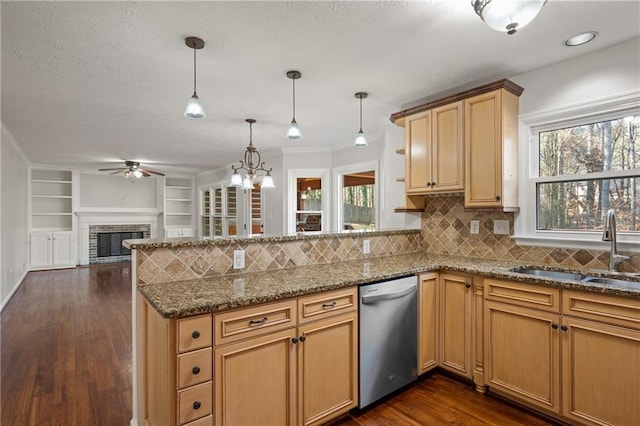 kitchen featuring sink, dishwasher, hanging light fixtures, a brick fireplace, and kitchen peninsula