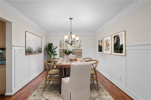 dining area with an inviting chandelier, crown molding, a decorative wall, and wood finished floors