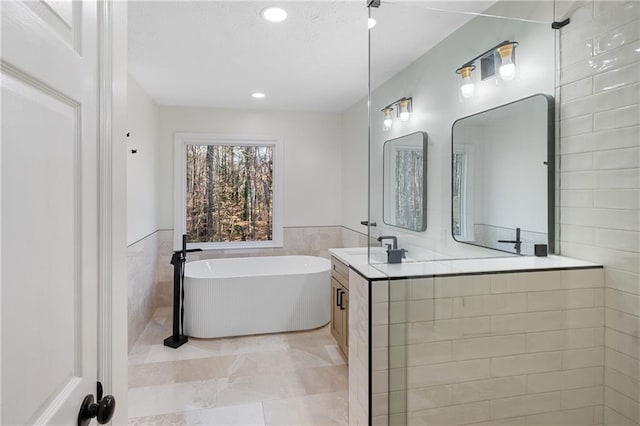 full bath with a wainscoted wall, a freestanding bath, vanity, tile walls, and recessed lighting