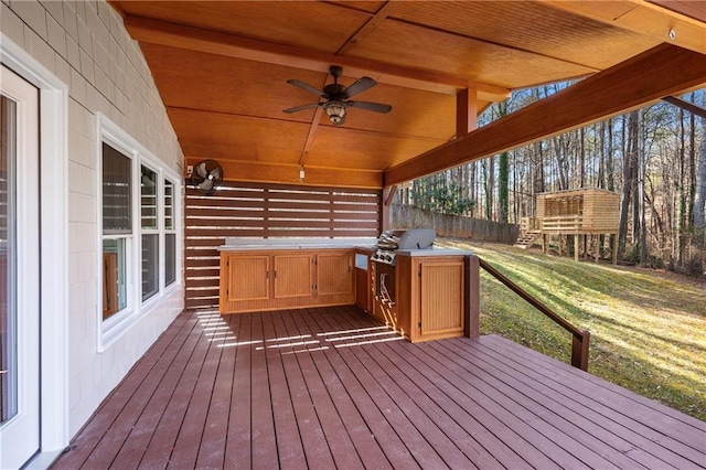 wooden deck with a lawn, ceiling fan, a grill, fence, and exterior kitchen