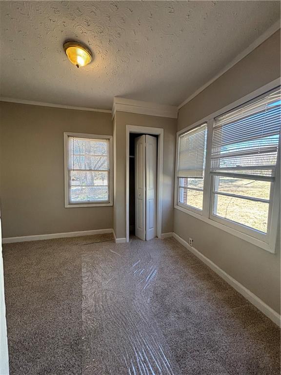 2103 River Rd, Ellenwood, GA 30294 - unfurnished bedroom with multiple windows, crown molding, a closet, a textured ceiling, and light colored carpet