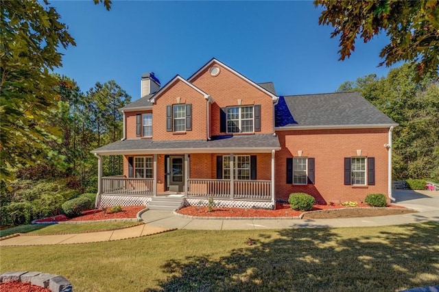 view of front of house featuring covered porch, a chimney, brick siding, and a front yard