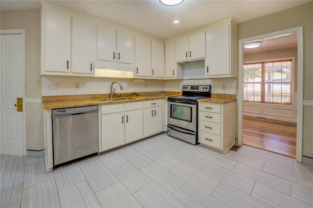 kitchen featuring tasteful backsplash, white cabinets, appliances with stainless steel finishes, light countertops, and a sink