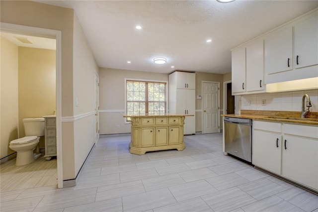 kitchen with a sink, backsplash, white cabinets, and stainless steel dishwasher