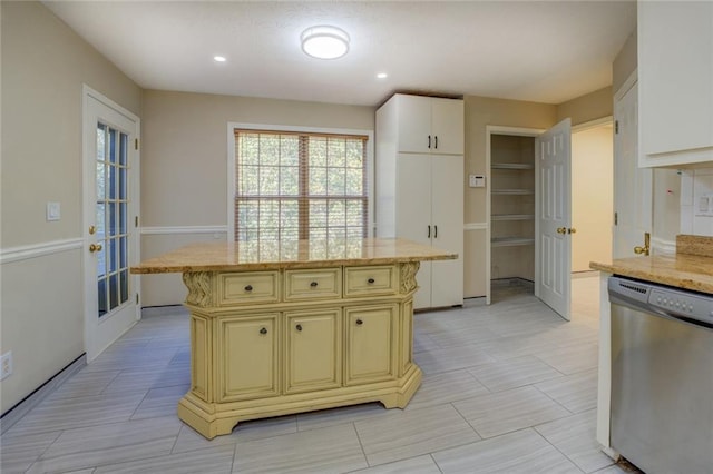 kitchen with recessed lighting, cream cabinets, stainless steel dishwasher, a kitchen island, and light stone countertops