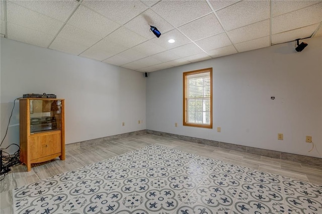 spare room featuring a paneled ceiling, light wood-style floors, and baseboards