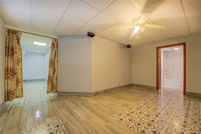 unfurnished room with light wood-type flooring, a drop ceiling, ceiling fan, and baseboards