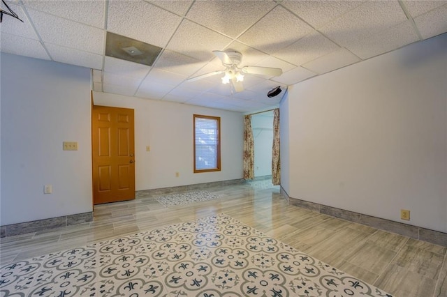 unfurnished room featuring light wood-type flooring, a drop ceiling, a ceiling fan, and baseboards