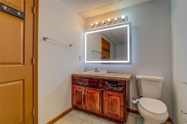 bathroom with toilet, vanity, a drop ceiling, baseboards, and tile patterned floors