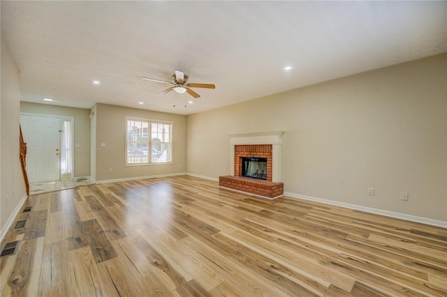 unfurnished living room with baseboards, a brick fireplace, and light wood-style floors