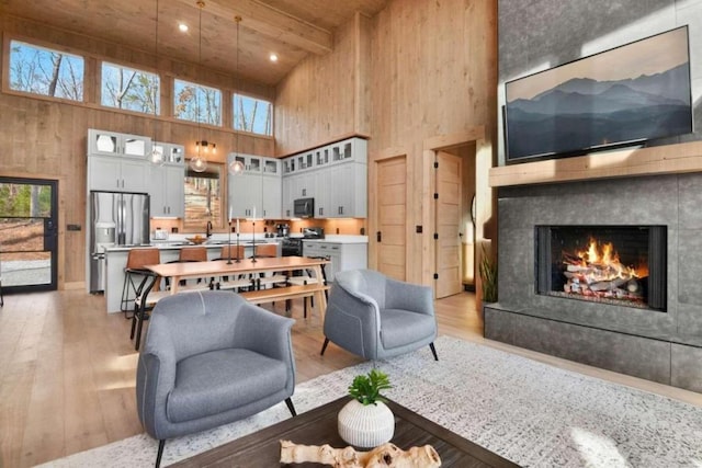 living room featuring a towering ceiling, a fireplace, beamed ceiling, wood ceiling, and light hardwood / wood-style flooring