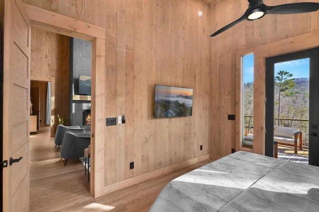 bedroom with access to exterior, wooden walls, light hardwood / wood-style floors, and ceiling fan