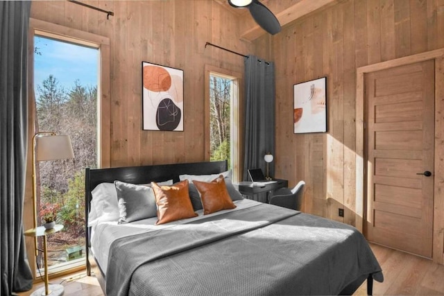 bedroom with multiple windows, light wood-type flooring, and wood walls